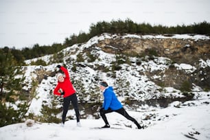 Senior couple runners stretching outside in winter nature.