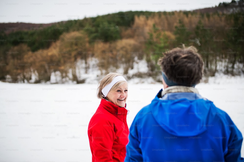 Senior couple runners standing outside in winter nature, resting.