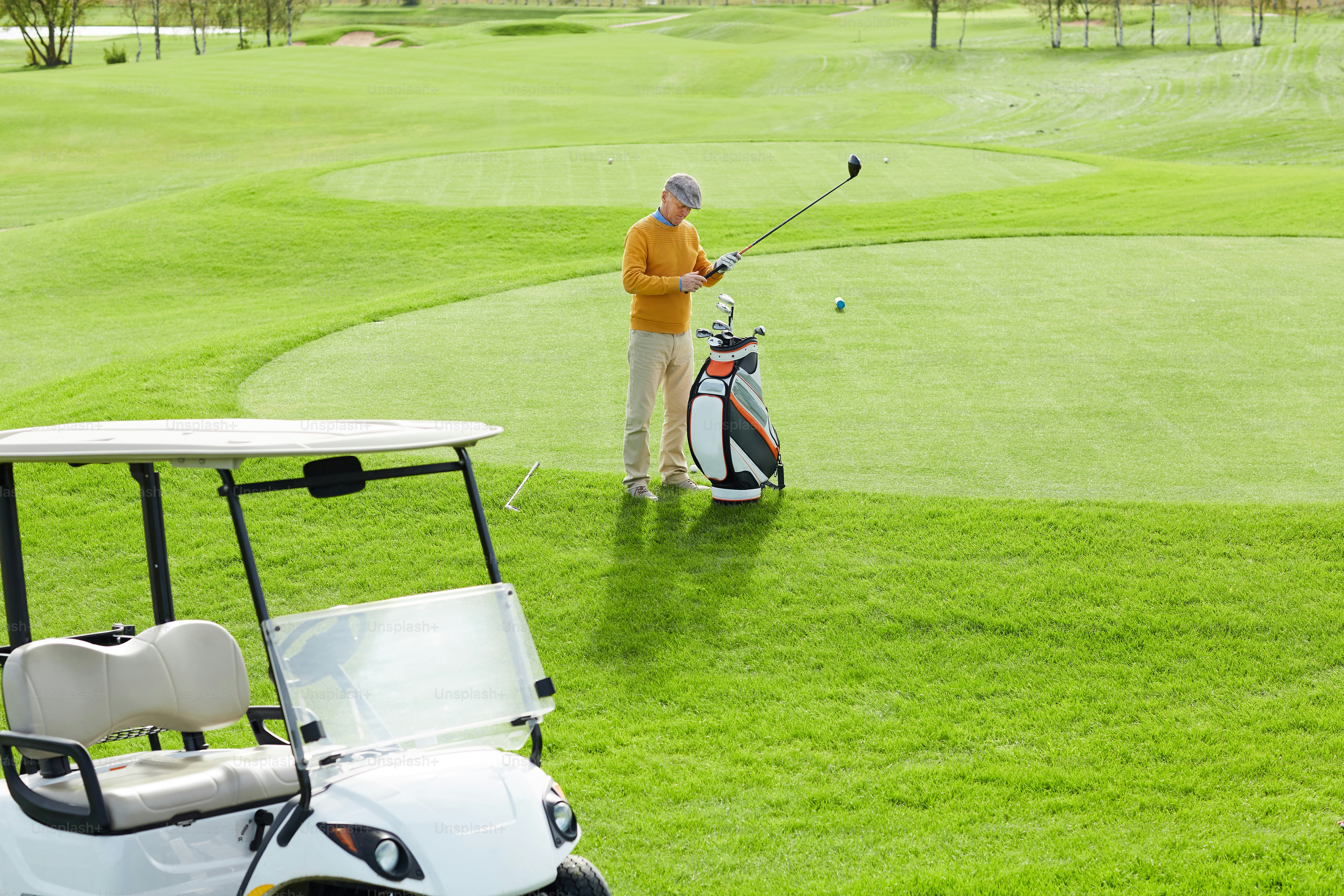 試合前に適当なゴルフクラブを選びながら、広い緑の野原の真ん中に立つカジュアルな男