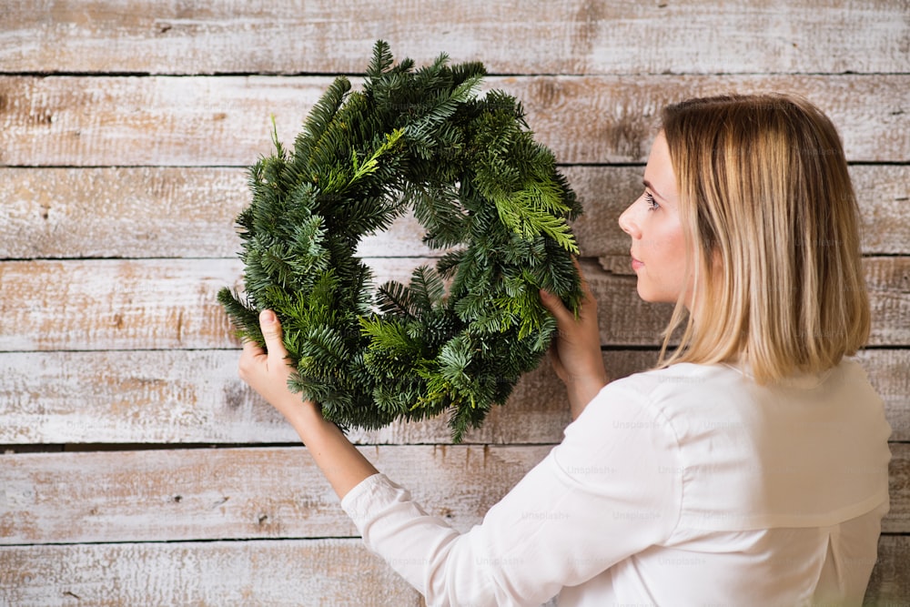 Young woman holding green wreath against wooden background. Christmas composition.