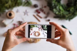 Christmas composition on a white background. Flat lay. Female hands holding a smartphone, taking a photograph.