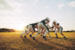 Grupo de jovens jogadores de futebol americano fazendo fila em formação durante uma sessão de treino em um campo esportivo em uma tarde ensolarada