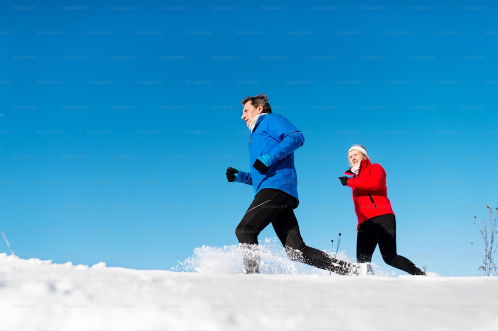 Une vue latérale d’un couple de personnes âgées heureux faisant du jogging dans la nature hivernale enneigée.