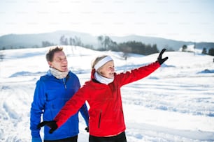 Senior couple runners standing outside in winter nature, resting.