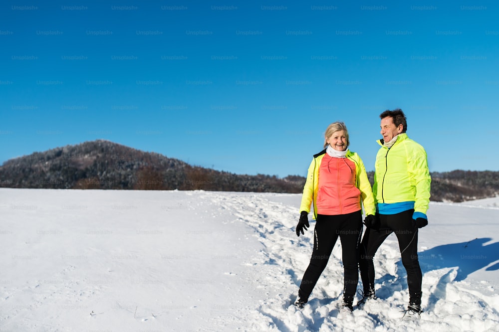 Senior couple runners standing outside in winter nature, resting. Copy space.