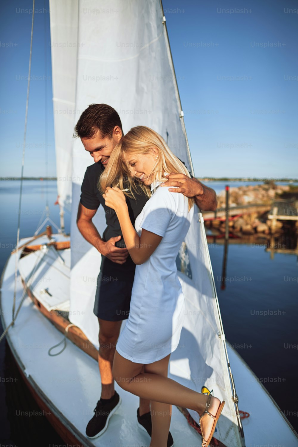 Laughing young husband and wife standing arm in arm together on the deck of their yacht while enjoying a sunny day sailing