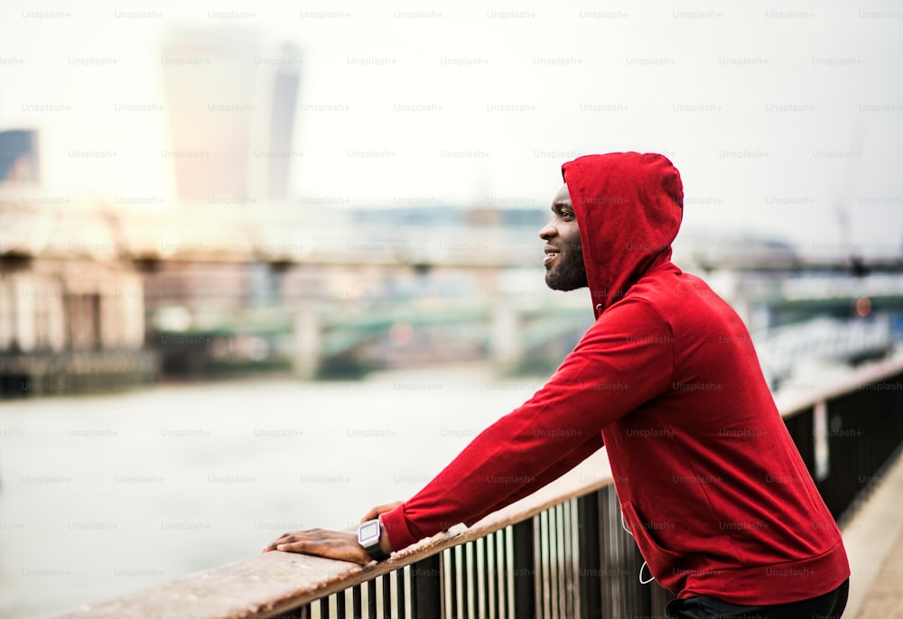 Junger sportlicher schwarzer Läufer ruht auf der Brücke draußen in einer Stadt.