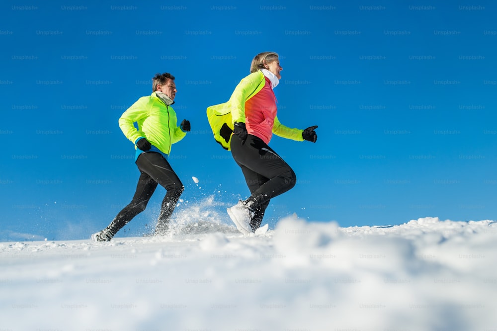 Senior couple runners running in winter nature in snow. Copy space.