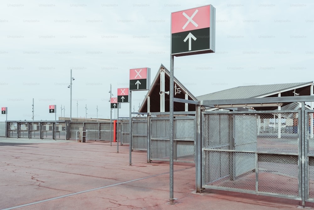Multiple checkpoint gates to the area where concerts or big sports events take place, plenty of poles with arrows and cross signs on the banners on the top, mesh fence stretching into the distance