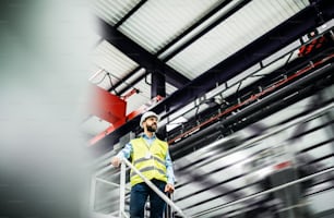 A low angle view of an industrial man engineer standing on the top of stairs in a factory. Copy space.