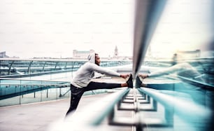 Young sporty black man runner on the bridge in a city, stretching.