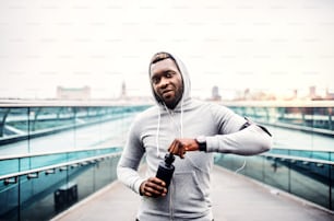 Ein junger sportlicher schwarzer Mann Läufer mit Smartwatch und Wasserflasche in einer Stadt.