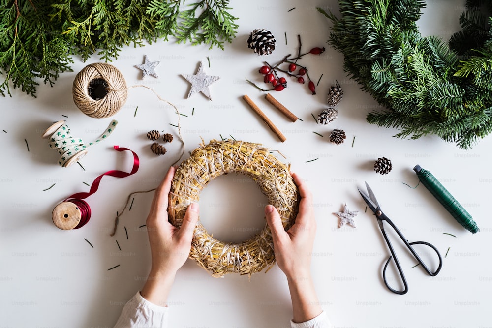 Christmas composition on a white background. Flat lay. Female hands holding wreath from straw.