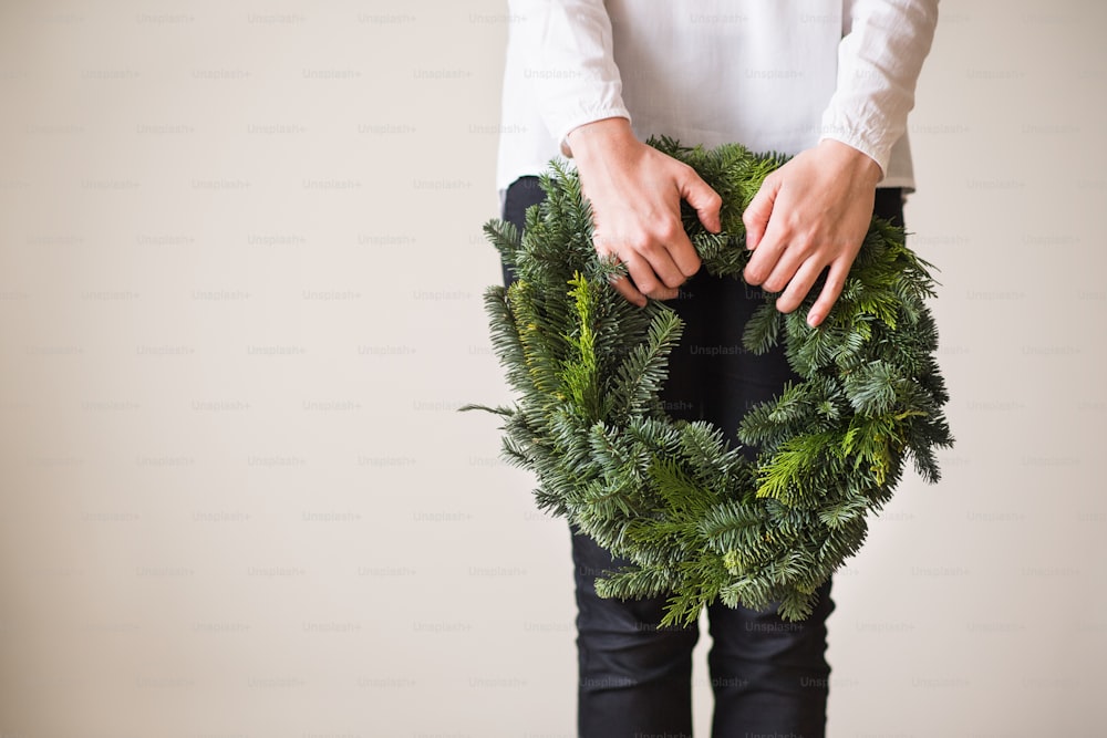 Unrecognizable woman holding green wreath. Christmas composition. Copy space.