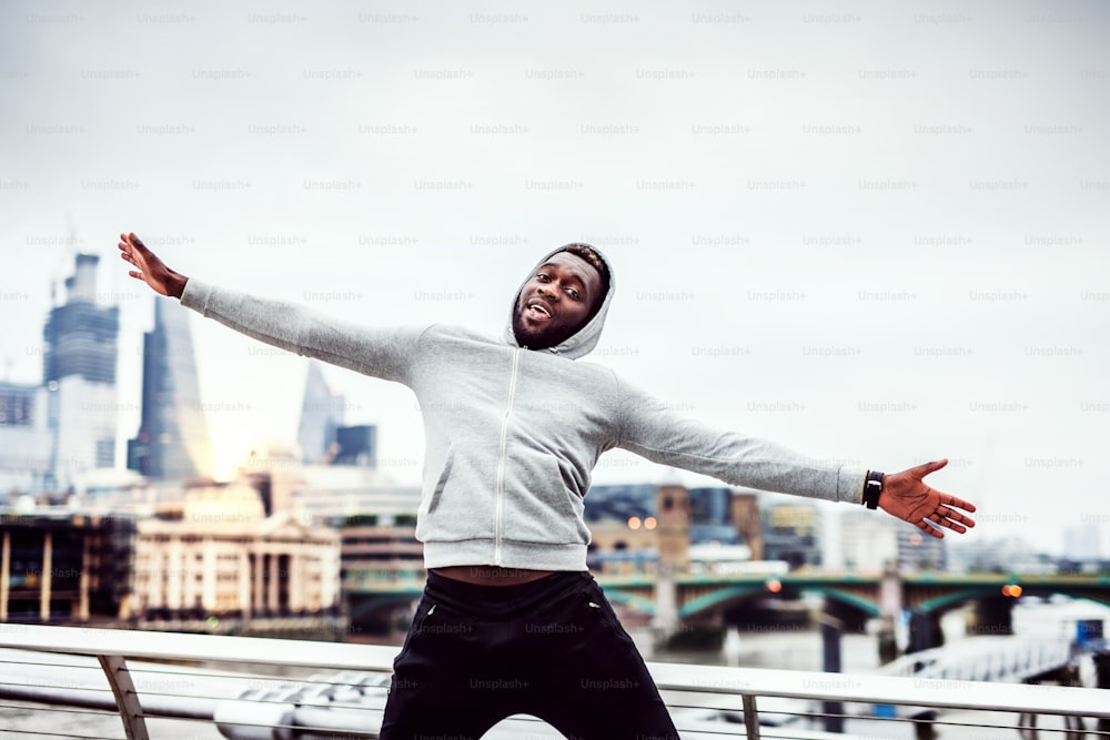 Young sporty black man runner with stretched out arms on the bridge in a city, resting and having fun.