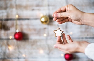 Female hand holding Christmas decorations. A star-shaped biscuit on a string. Copy space.
