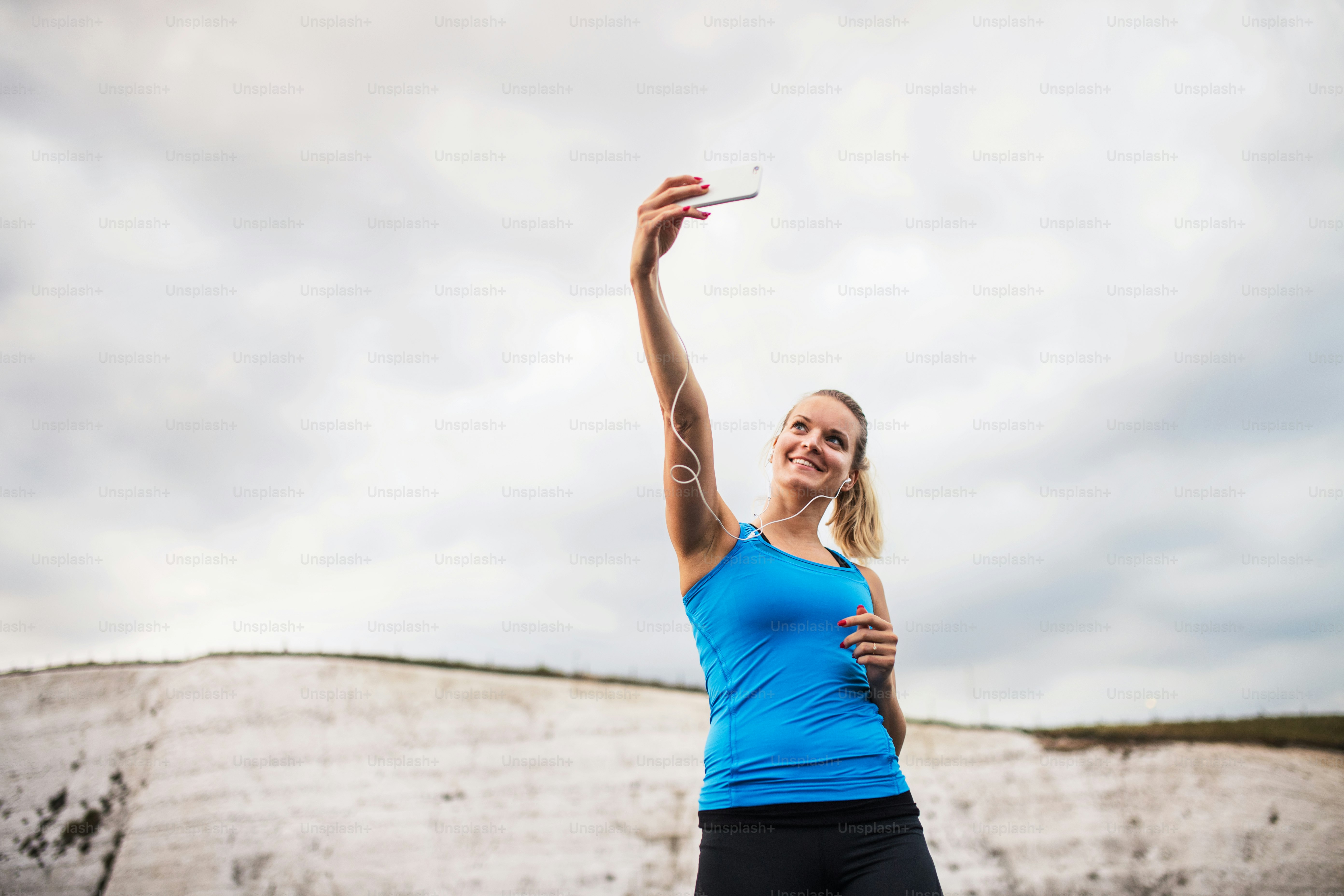 ビーチでイヤホンとスマートフォンを持ち、自撮りをする若いスポーティな女性ランナー。スペースをコピーします。