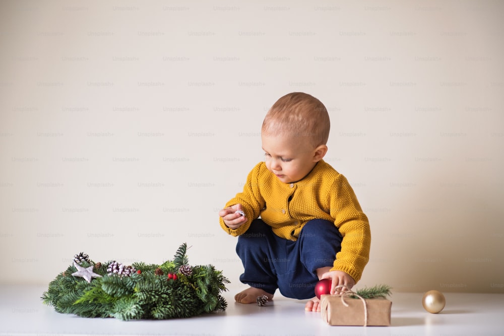 A toddler boy, wrapped present and a Christmas wreath on a table.
