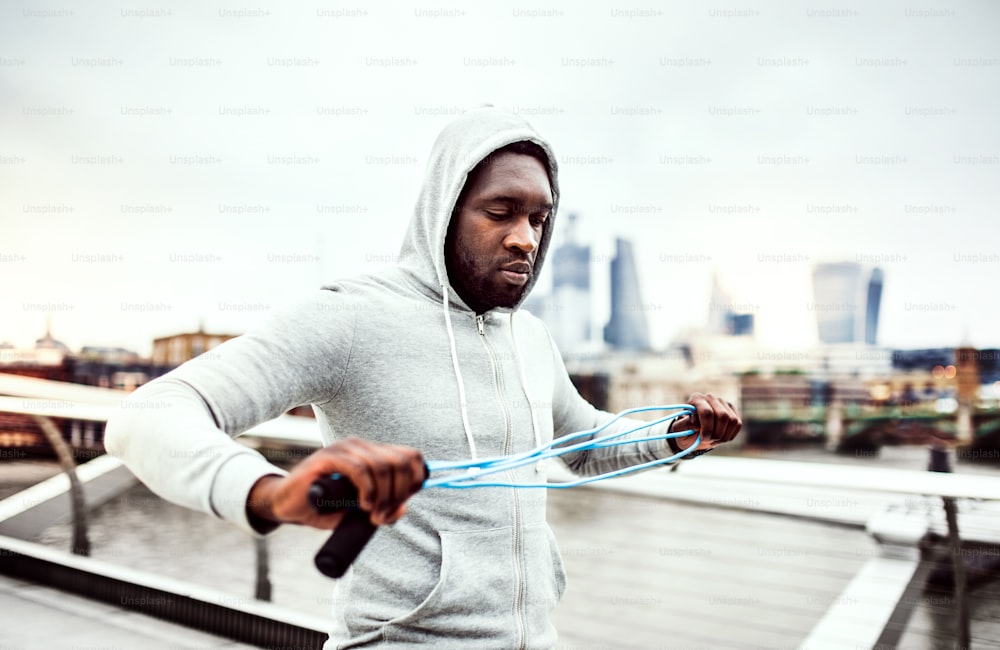 Young active handsome black sportsman with skipping rope in a city, wearing hoodie.