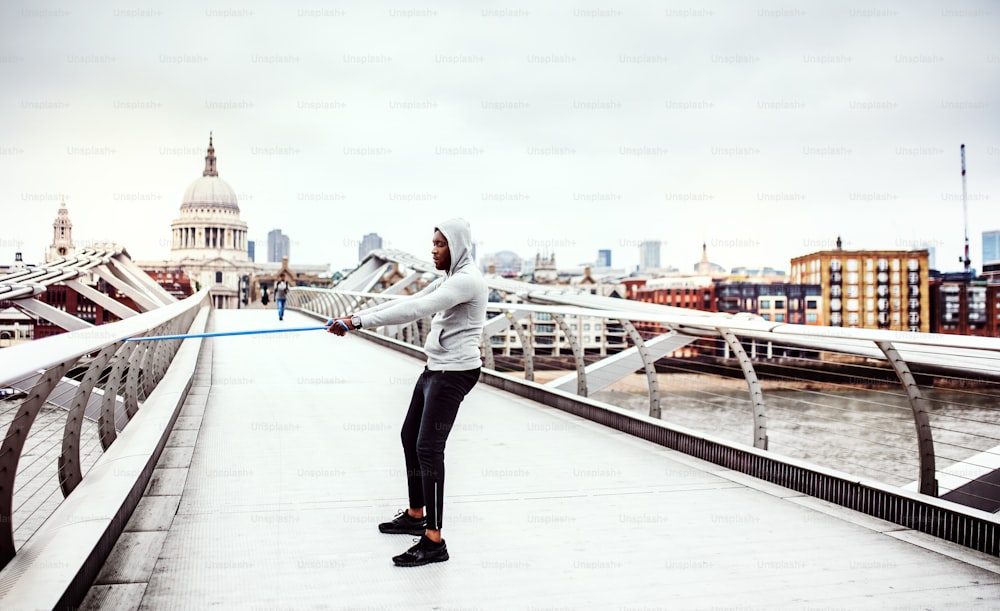 Joven deportista negro activo haciendo ejercicio con bandas elásticas de goma en el puente de Londres, la catedral de San Pablo en el fondo.