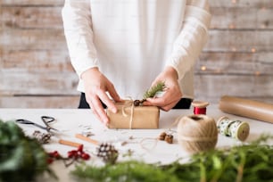 Weihnachtskomposition auf weißem Hintergrund. Weibliche Hände schmücken ein eingepacktes Geschenk.