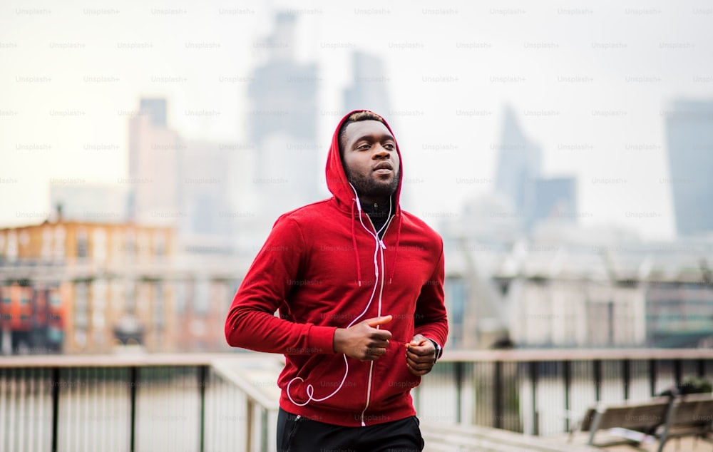 Young sporty black man runner with earphones running on the bridge outside in a city.