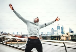 Young sporty black man runner with stretched out arms on the bridge in a city, resting and having fun.