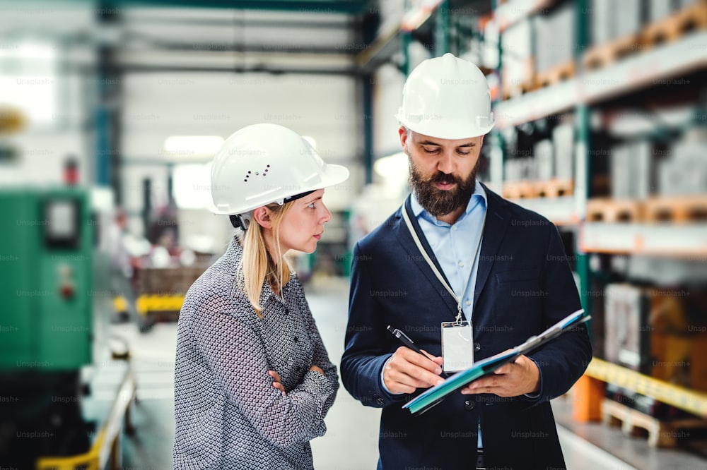A portrait of a serious mature industrial man and woman engineer with clipboard in a factory, working.