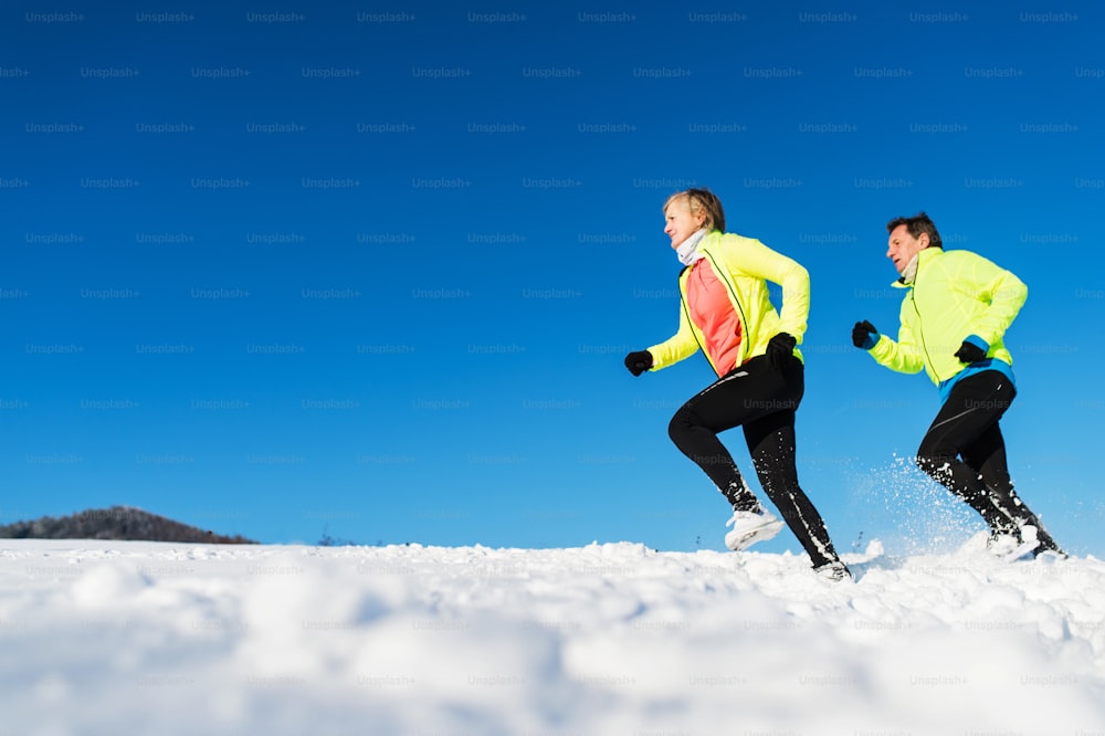 Coppia di corridori anziani che corrono nella natura invernale nella neve. Copia spazio.
