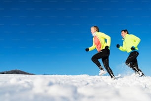 Senior couple runners running in winter nature in snow. Copy space.