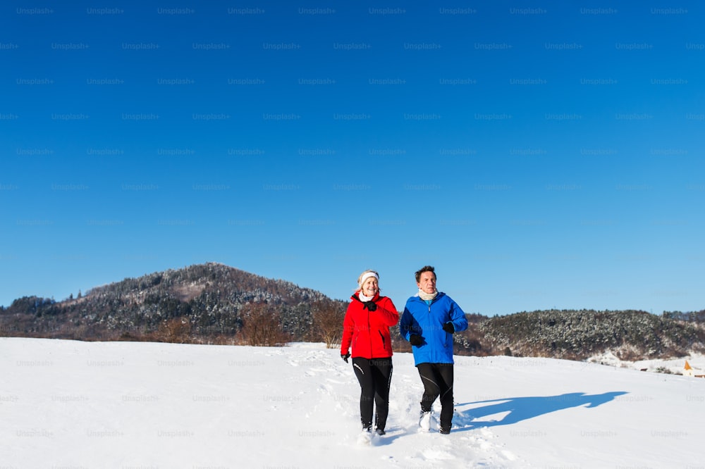 Active happy senior couple jogging in snowy winter nature.