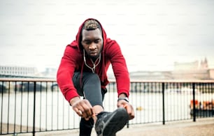 A young sporty black man runner tying shoelaces before running outside in a city.