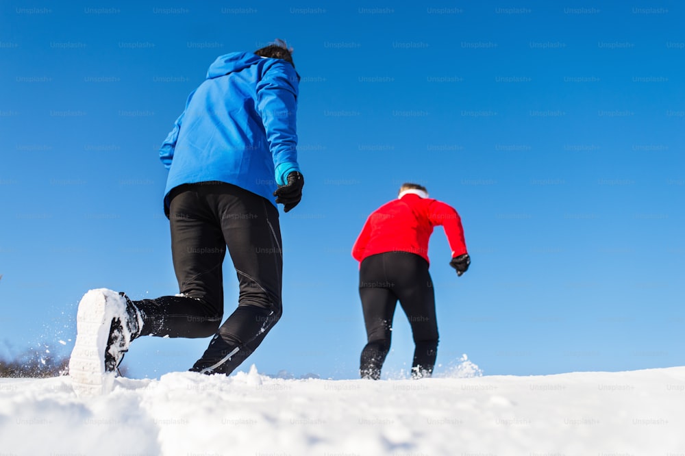 Una vista posteriore di una coppia anziana attiva che fa jogging nella natura invernale innevata.