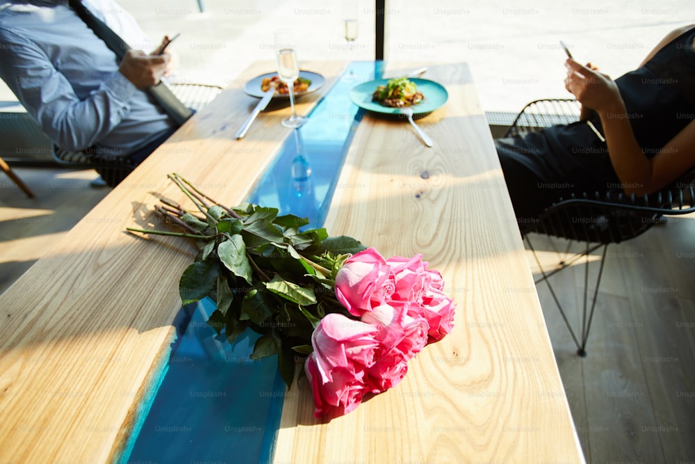 Roses roses fraîches sur la table avec de la nourriture servie et un couple accro aux gadgets sur fond