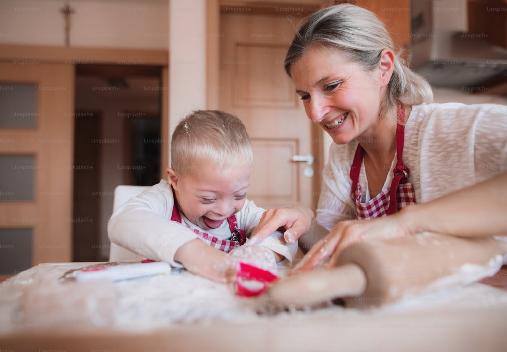 Un bambino handicappato felice con la sindrome di Down e sua madre in casa a cuocere in una cucina.