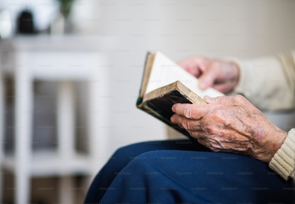 Un gros plan des mains et des genoux d’une femme âgée lisant la Bible à la maison.