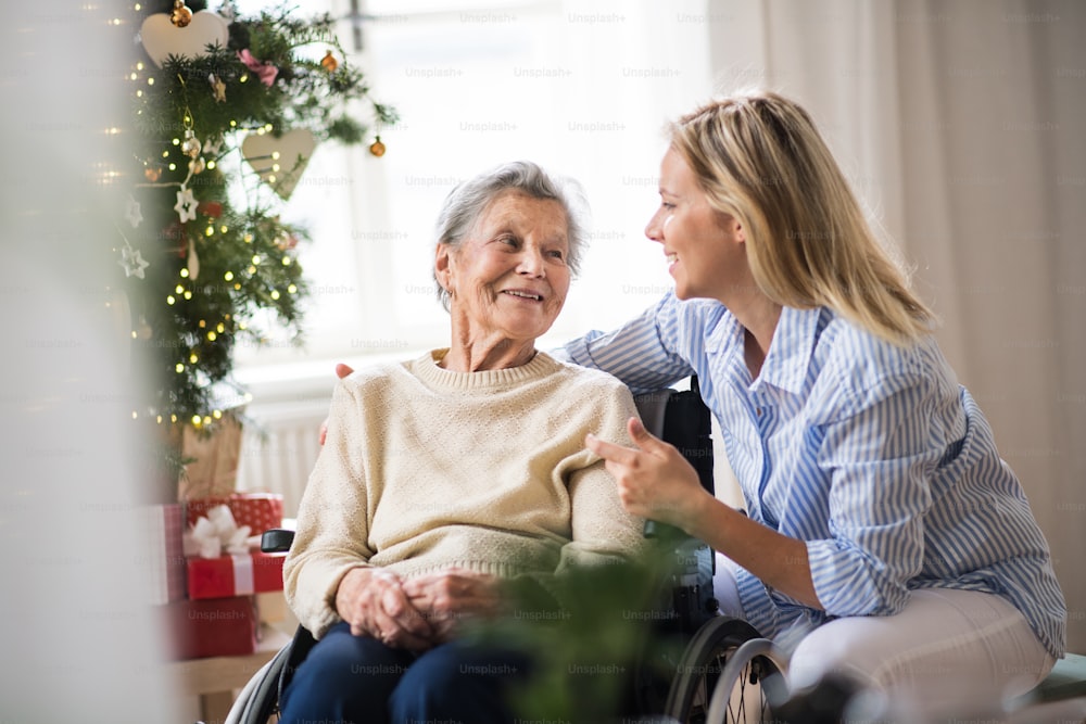 Una anciana en silla de ruedas con un visitador sanitario en casa en Navidad, hablando.