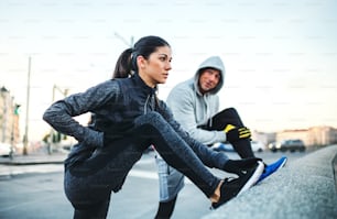 A fit sporty couple runners doing stretching outdoors on the bridge in Prague city, Czech Republic.