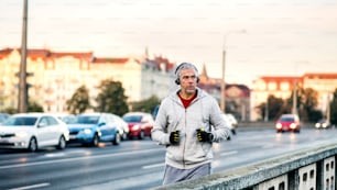Un corredor masculino maduro en forma con auriculares corriendo al aire libre en el puente de la ciudad de Praga, escuchando música.