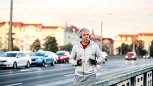 A fit mature male runner with headphones running outdoors on the bridge in Prague city, listening to music.