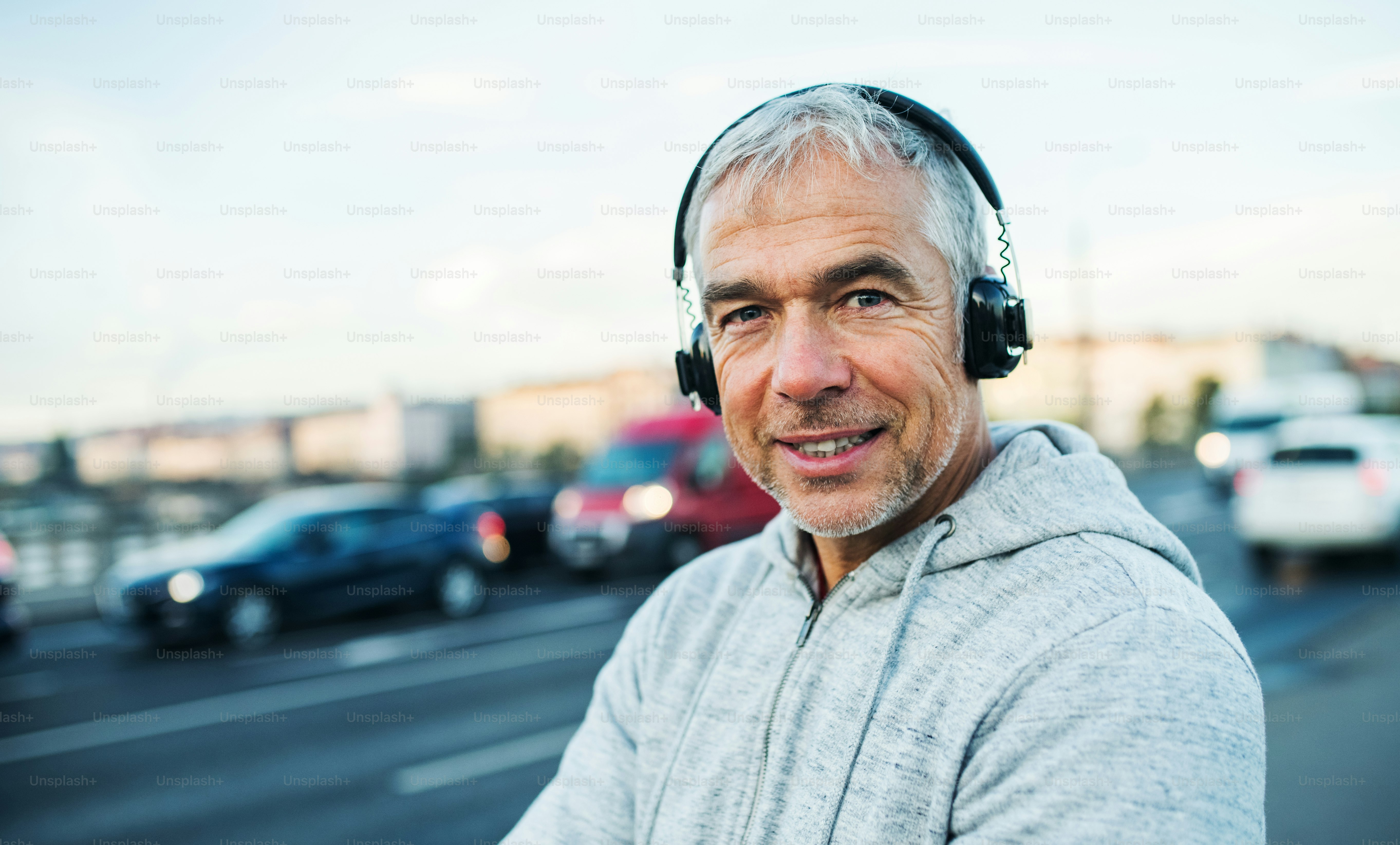 Mature male runner with black headphones outdoors on the bridge in Prague city, listening to music.