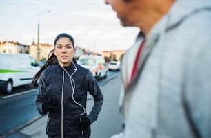 A fit young female runner with earphones running outdoors on the bridge in Prague city, listening to music.
