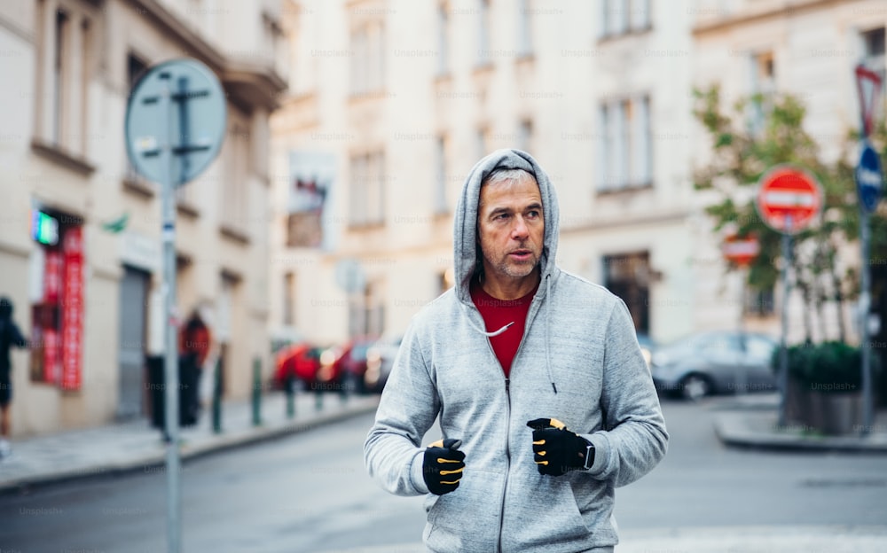 Mature male runner with gloves running outdoors on the street in Prague city.