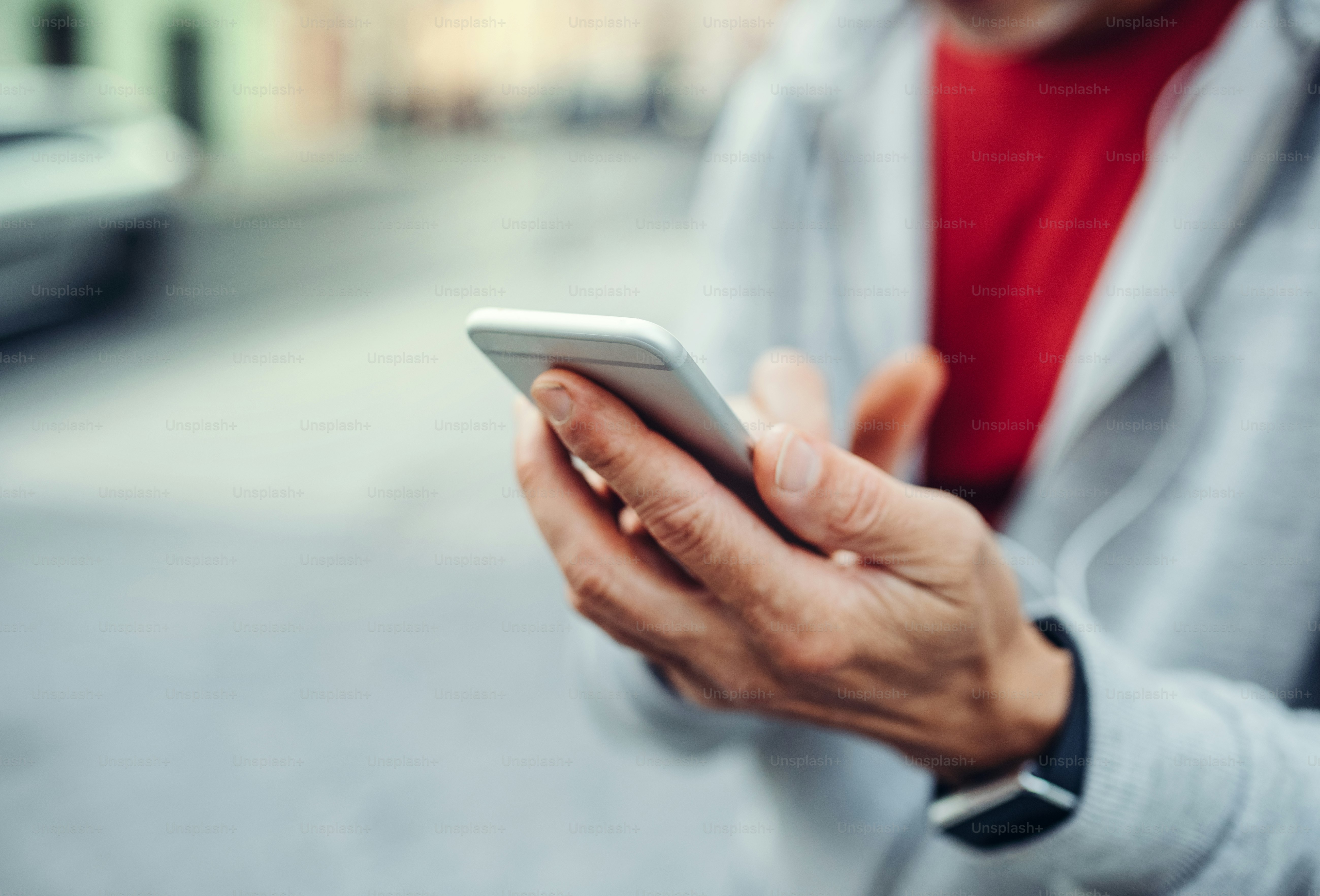A close-up of hands of unrecognizable man standing outdoors in city, using smartphone.