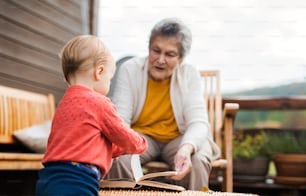 An elderly woman with a toddler great-grandchild on a terrace on a sunny day in autumn.