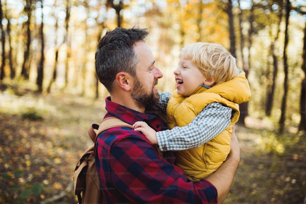 A mature father standing and holding a toddler son in an autumn forest, talking.