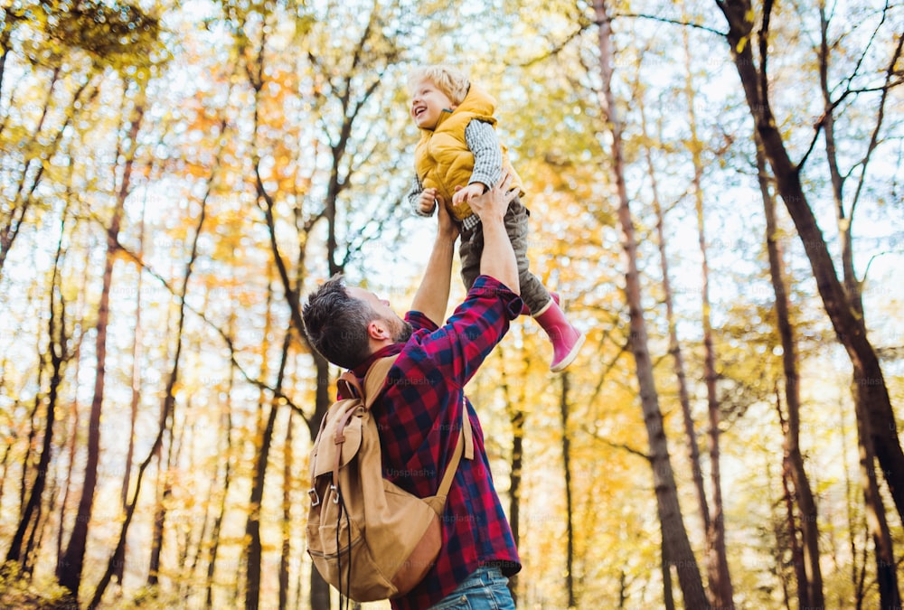 A mature father lifting a happy toddler son in the air in an autumn forest.