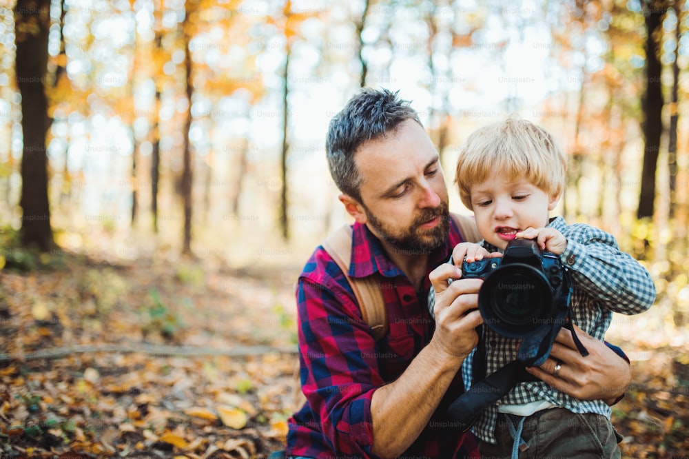 A mature father and a toddler son in an autumn forest, taking pictures with a digital camera.