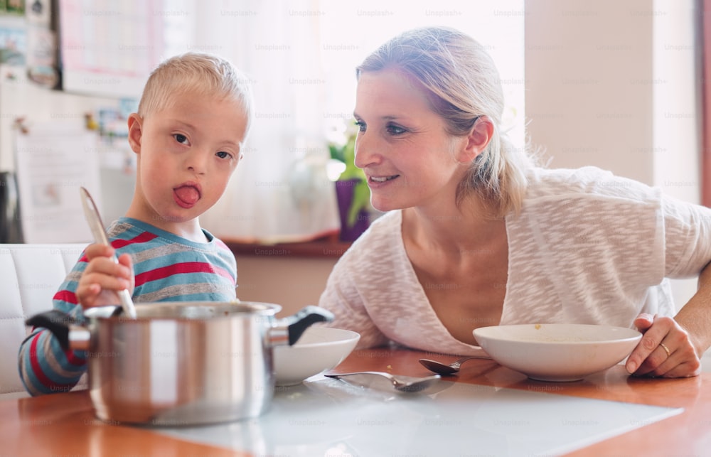 Uma criança deficiente com síndrome de down com sua mãe dentro de casa almoçando ou jantando.