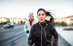 A fit sporty couple with headphones running outdoors on the bridge in Prague city, listening to music.